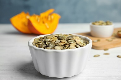 Photo of Bowl of raw pumpkin seeds on white wooden table