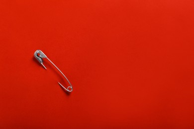 Safety pin attached on red paper, top view. Space for text