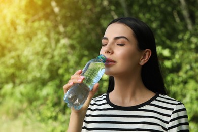 Beautiful young woman drinking water outdoors. Refreshing drink