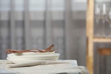 Photo of Stacked clean dishes, cutlery and towel on table indoors