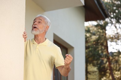 Photo of Angry senior man showing fist near house, space for text. Annoying neighbour