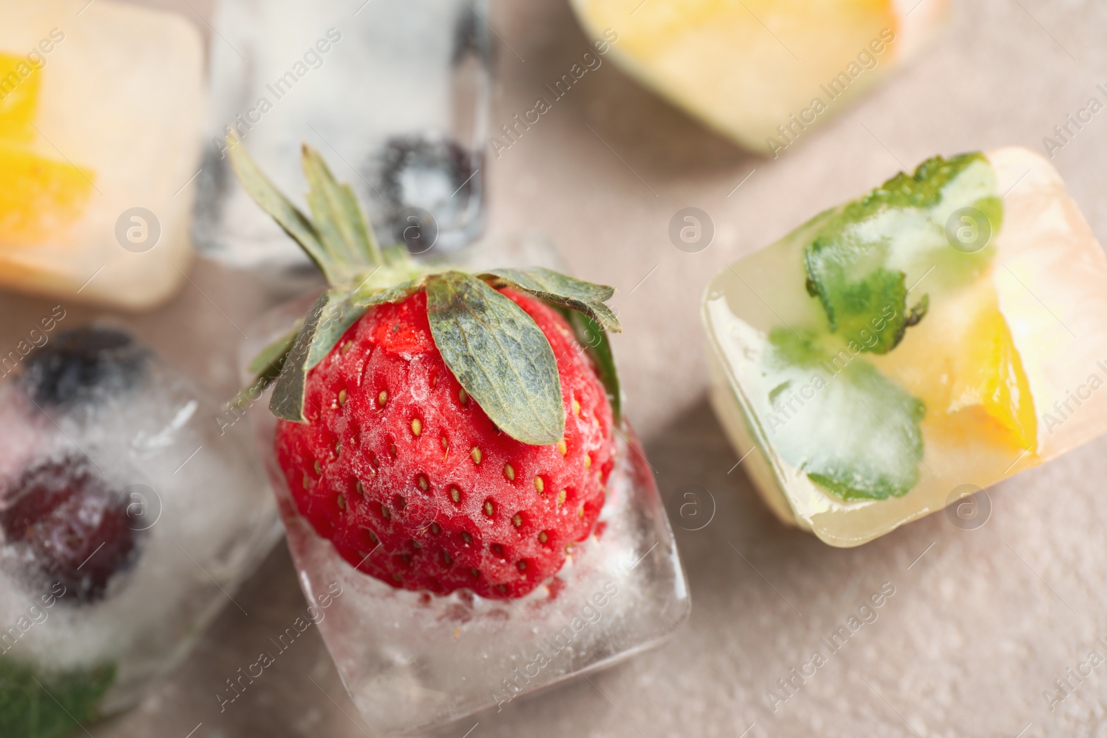 Photo of Ice cubes with different berries and mint on grey table, closeup