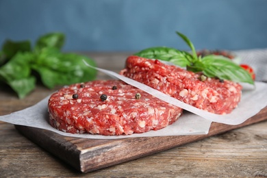 Photo of Raw meat cutlets for burger on wooden table against blue background, closeup