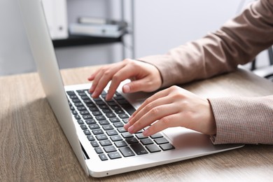 Photo of Woman working on laptop at wooden table in office, closeup