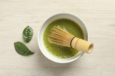 Photo of Cup of fresh matcha tea with bamboo whisk and leaves on white wooden table, flat lay