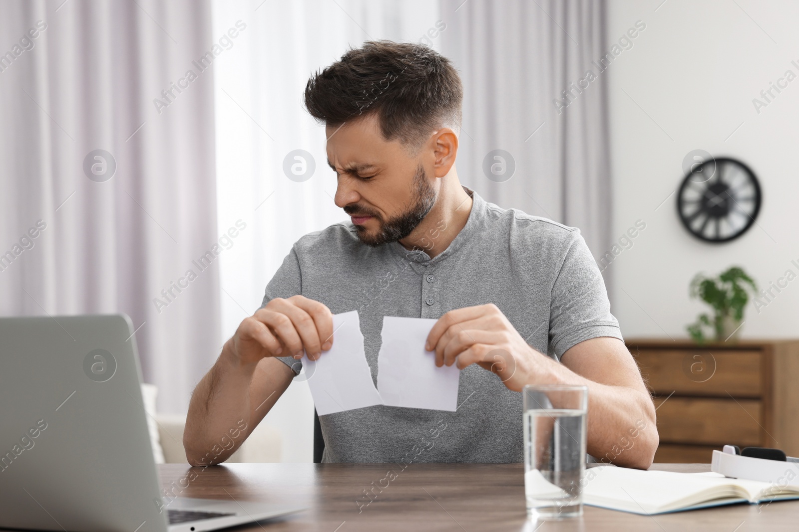 Photo of Man ripping photo at table indoors. Divorce concept