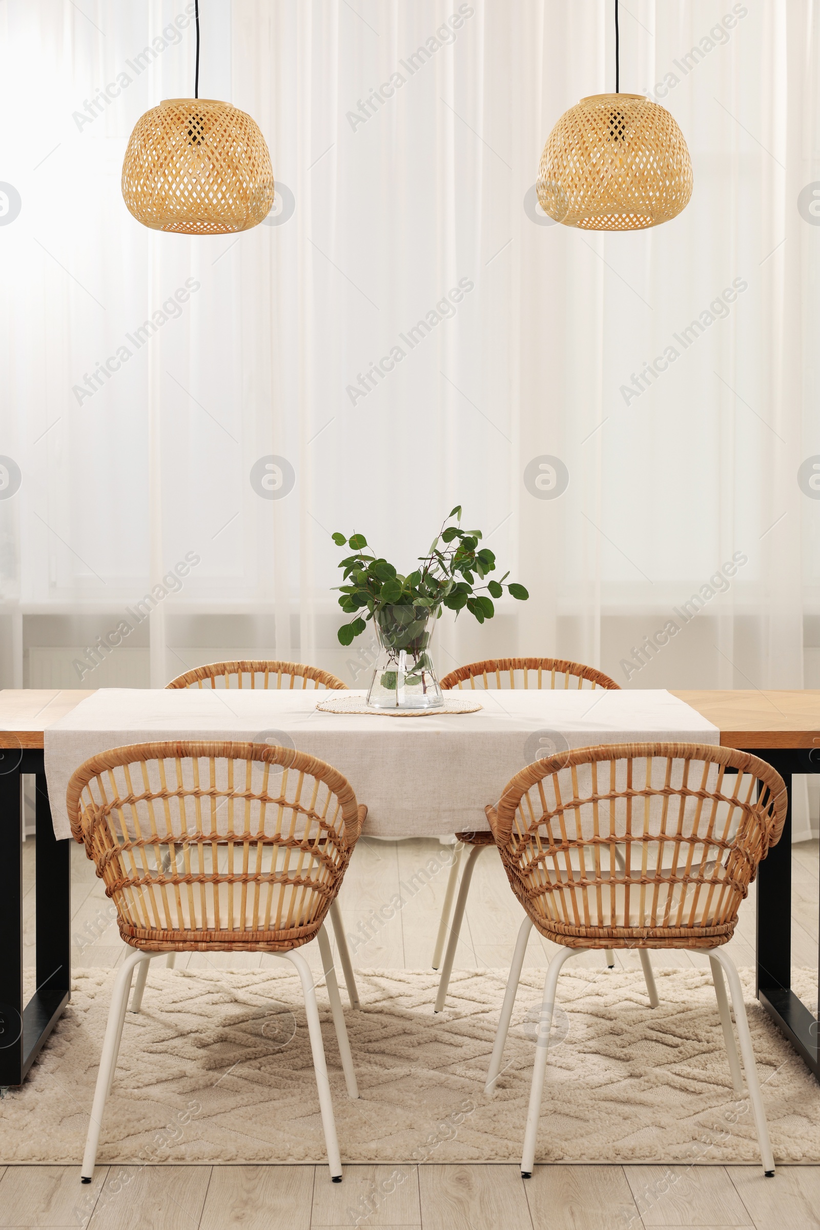 Photo of Vase with eucalyptus branches on table and chairs in dining room