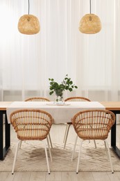 Photo of Vase with eucalyptus branches on table and chairs in dining room