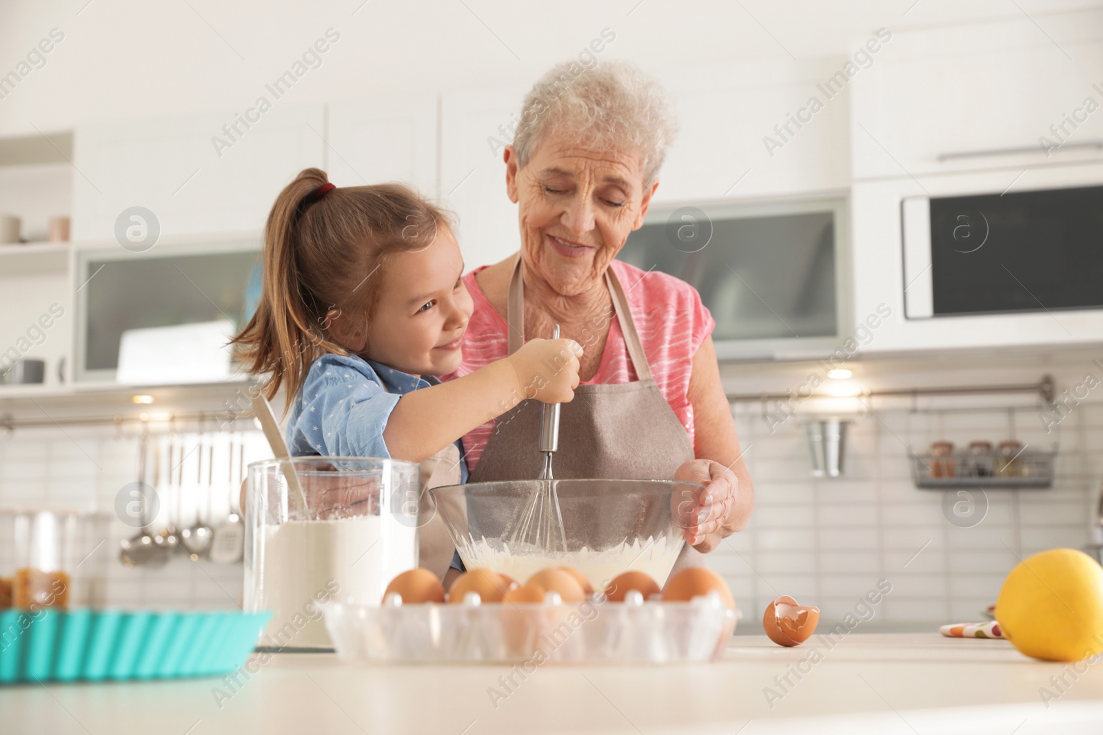 Photo of Cute girl and her grandmother cooking in kitchen