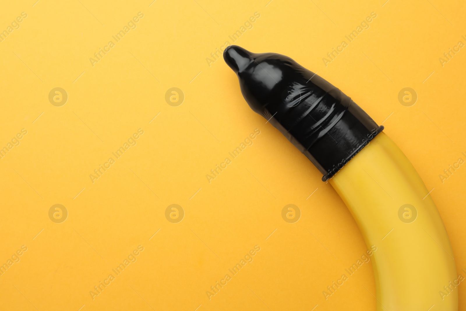 Photo of Banana with condom on orange background, top view and space for text. Safe sex concept