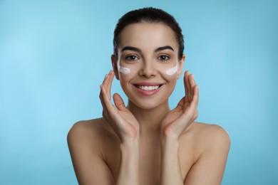 Photo of Young woman applying facial cream on light blue background
