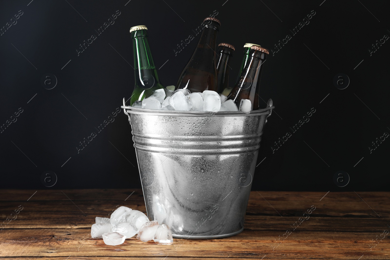 Photo of Metal bucket with bottles of beer and ice cubes on wooden table