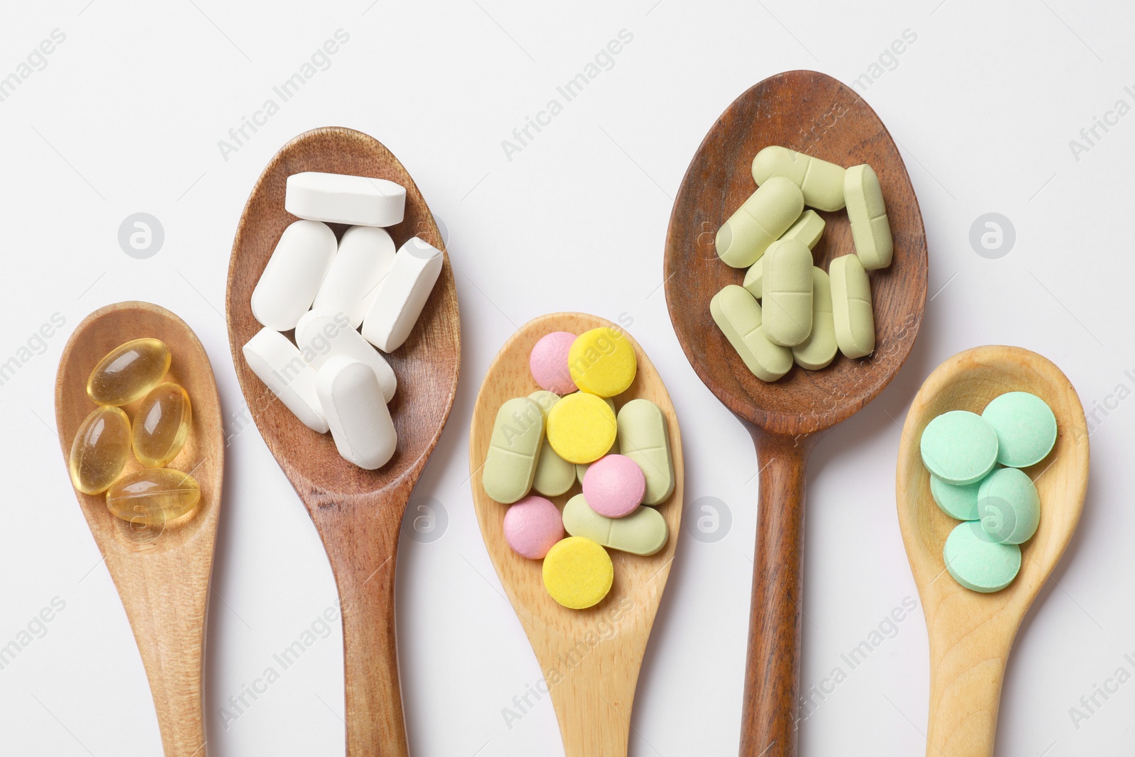 Photo of Different vitamin pills in wooden spoons on white background, flat lay