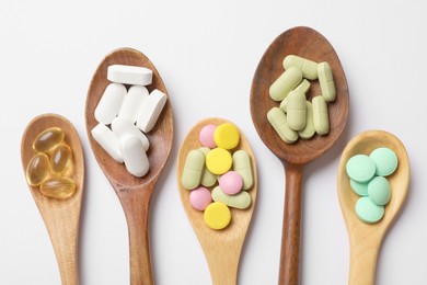 Different vitamin pills in wooden spoons on white background, flat lay