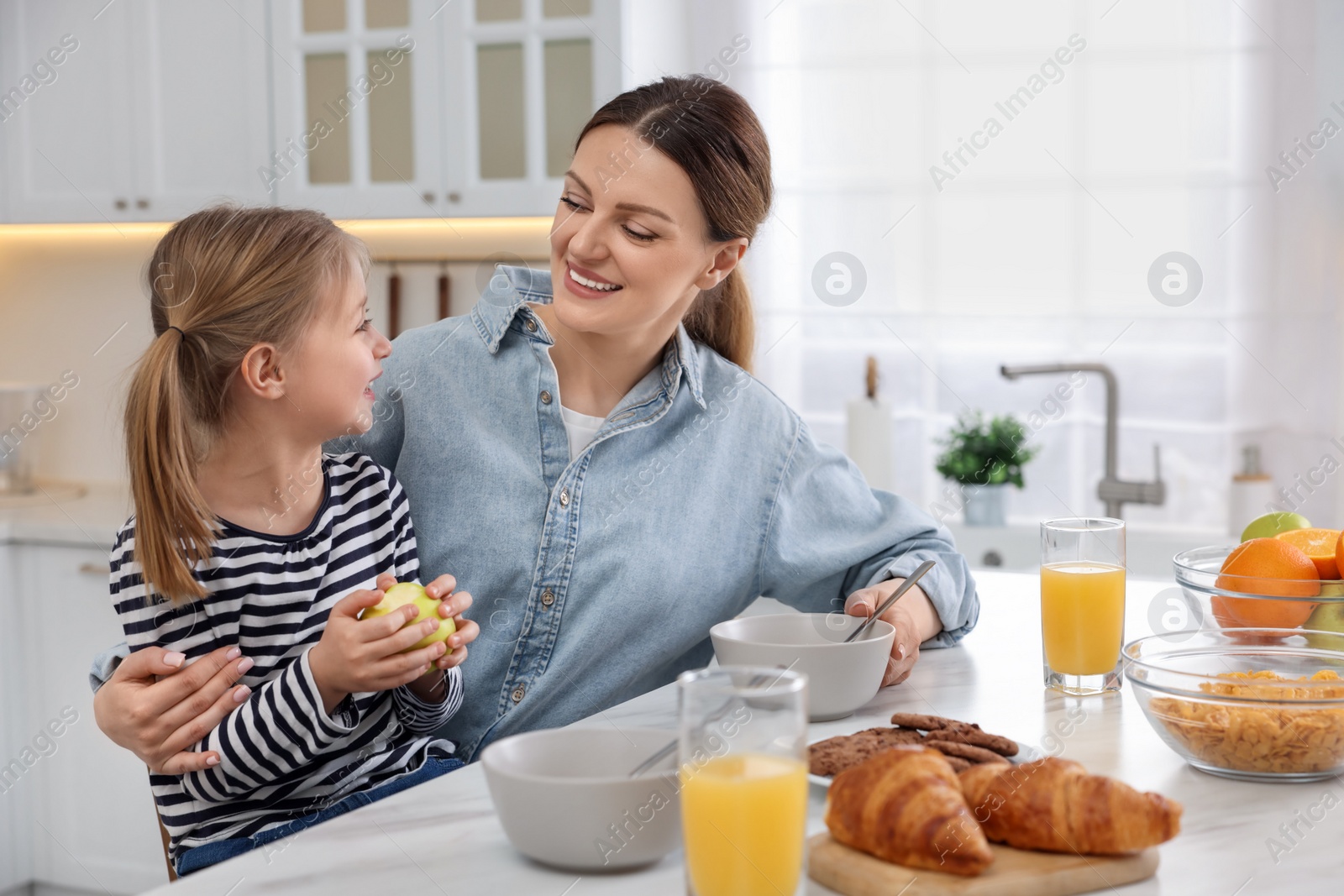 Photo of Mother and her cute little daughter having breakfast at table in kitchen