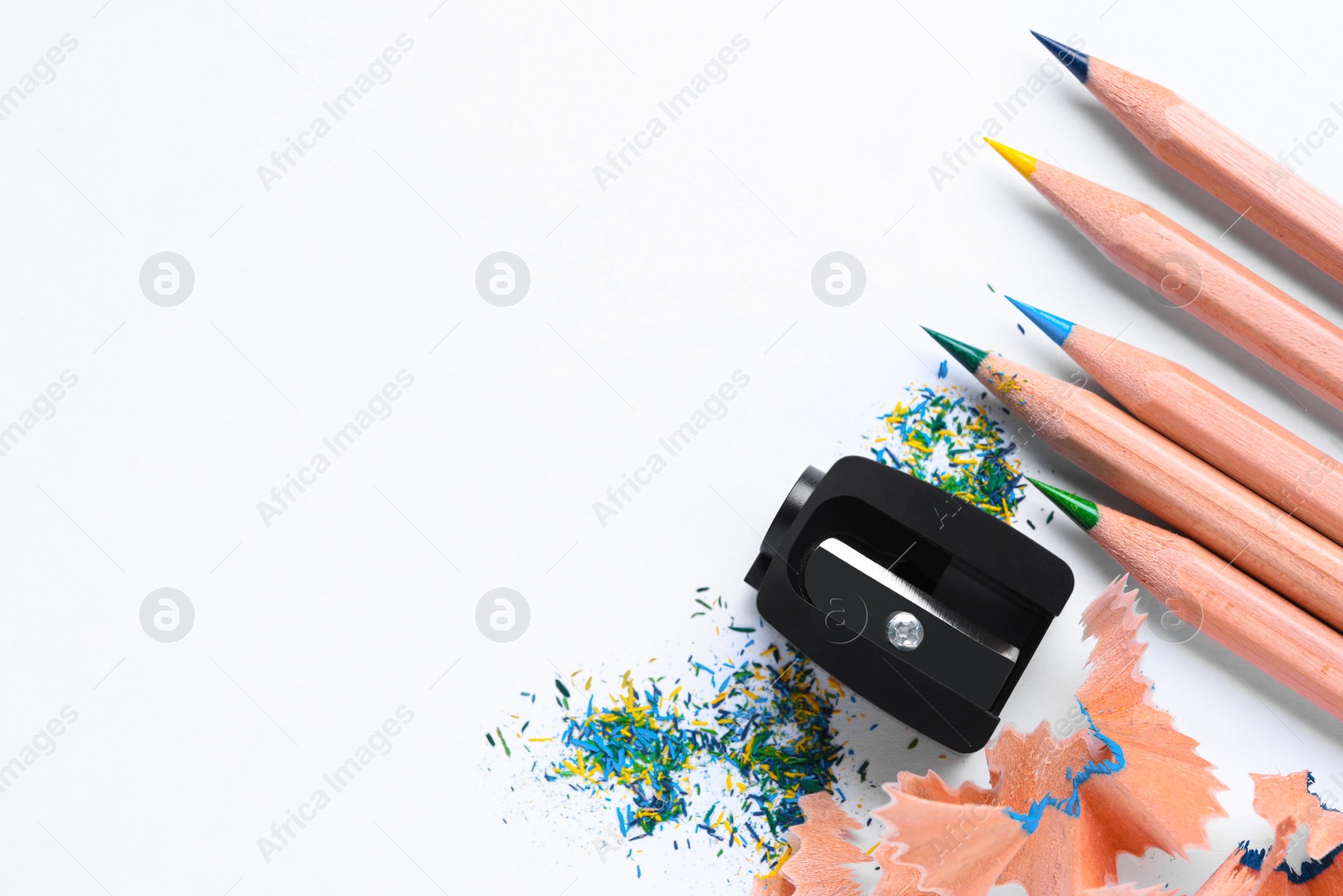 Photo of Colorful pencils, sharpener and shavings on white background, flat lay. Space for text