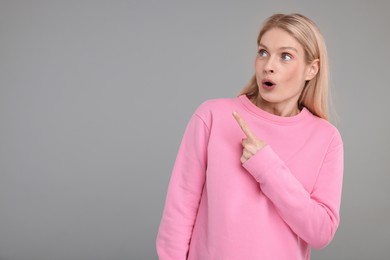 Photo of Surprised woman pointing at something on grey background, space for text