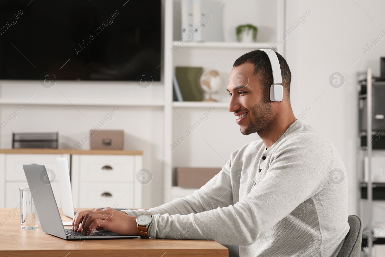 Photo of Young man with headphones working on laptop at table in office