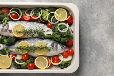 Photo of Raw fish with vegetables and lemon in baking dish on grey textured table, top view. Space for text