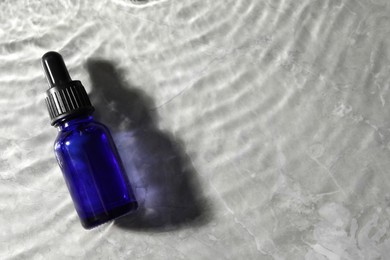 Photo of Bottle of face serum in water on light background, top view. Space for text