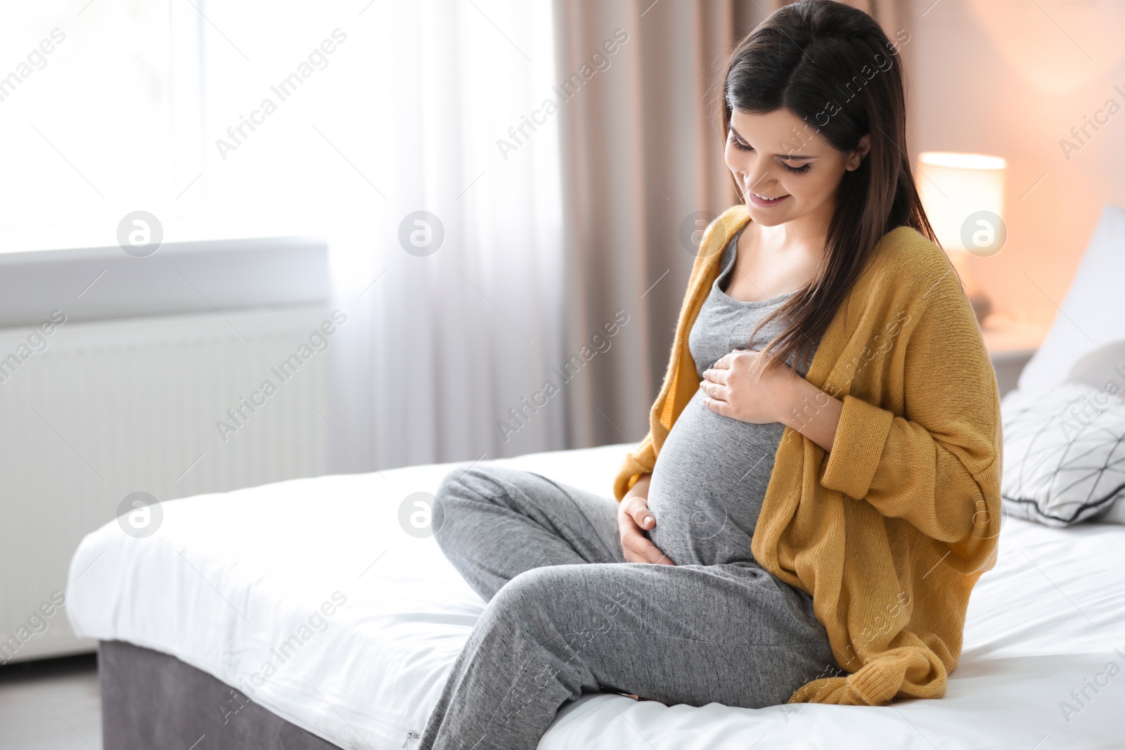 Photo of Young pregnant woman sitting on bed at home