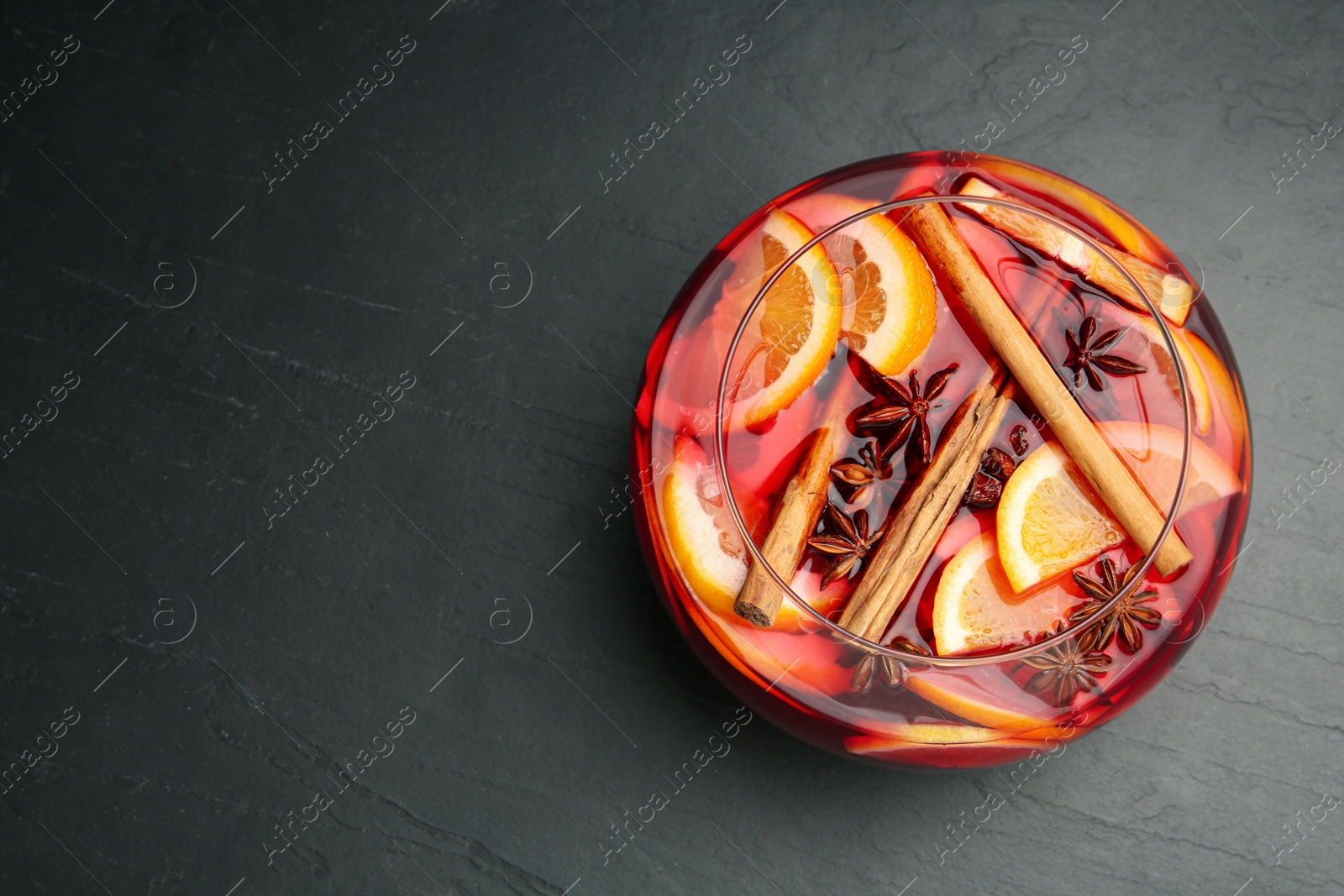 Photo of Glass bowl of delicious aromatic punch drink on black table, top view. Space for text