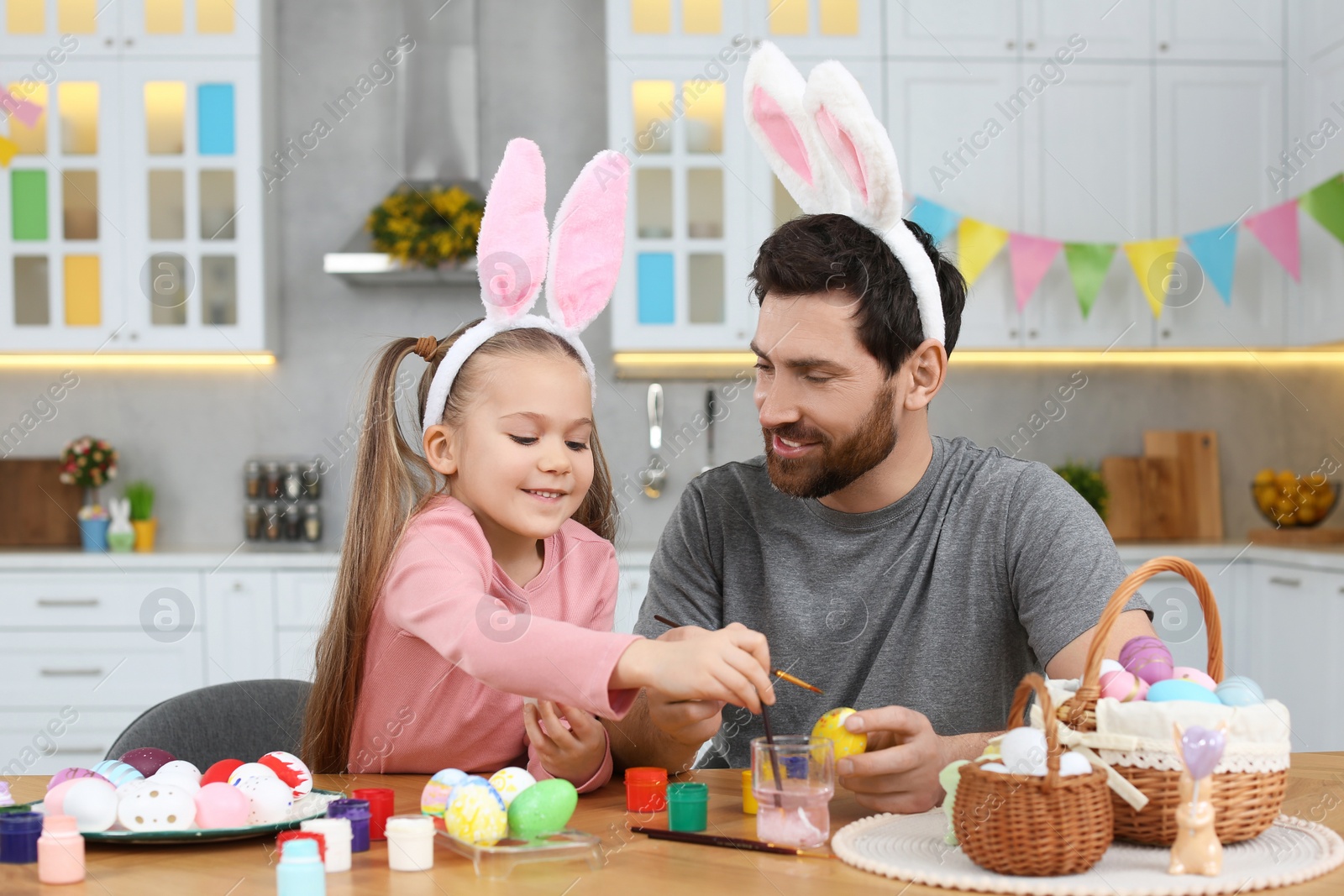 Photo of Father and his cute daughter painting Easter eggs at table in kitchen