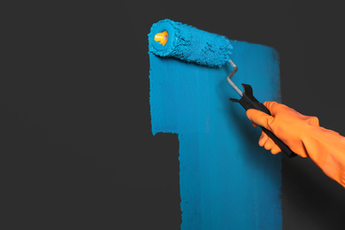 Photo of Woman painting grey wall with blue dye, closeup. Space for text