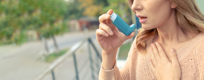 Image of Closeup view of woman using asthma inhaler outdoors, space for text. Banner design