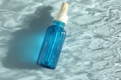 Wet bottle of cosmetic serum on light blue background, top view. Space for text