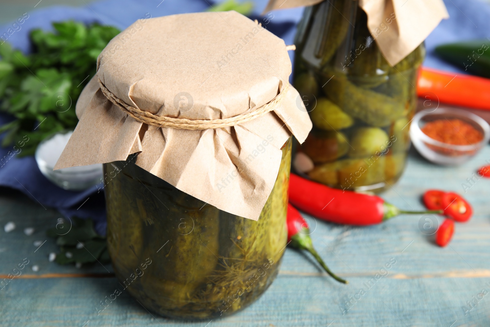 Photo of Jars with pickled cucumbers on blue wooden table, closeup view