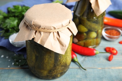 Photo of Jars with pickled cucumbers on blue wooden table, closeup view