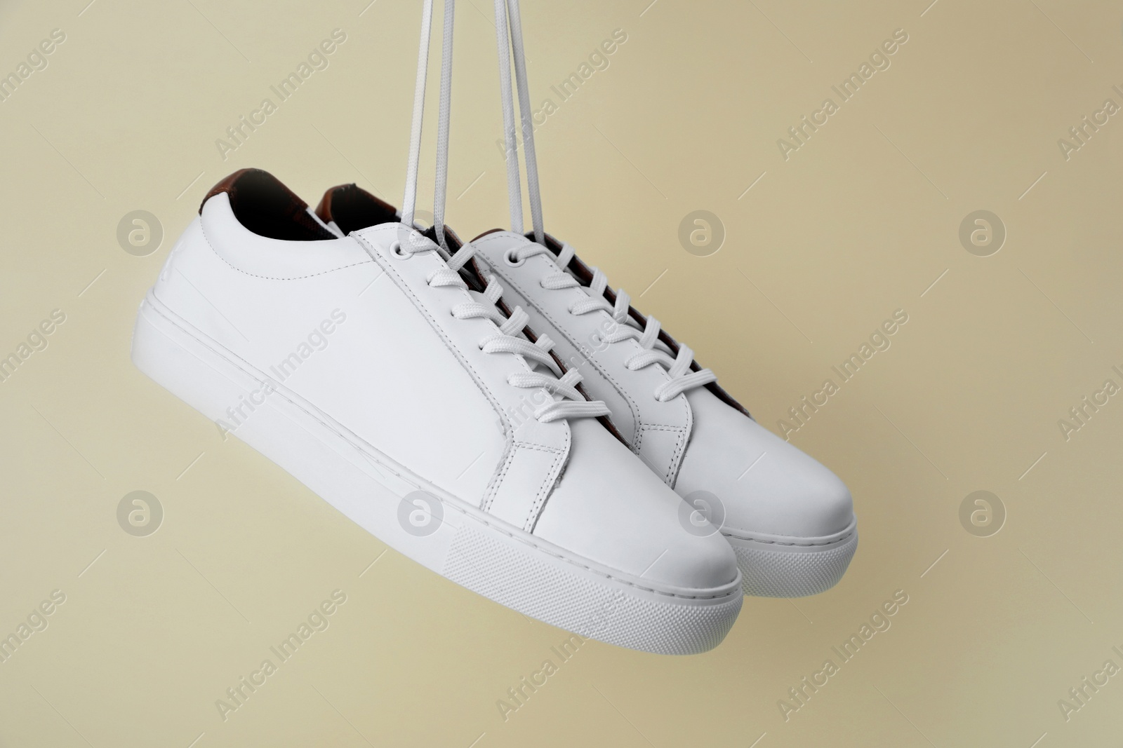 Photo of Pair of stylish sports shoes hanging on beige background