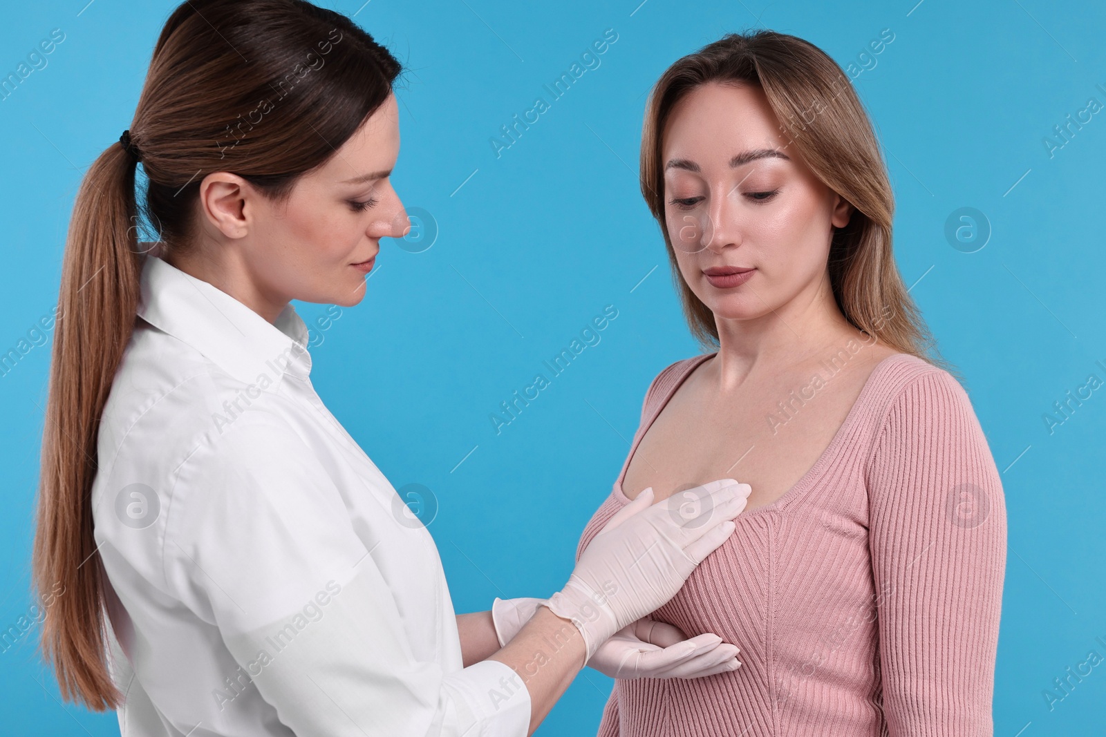 Photo of Mammologist checking woman's breast on light blue background