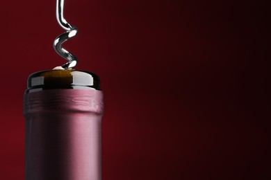 Photo of Opening bottle of wine with corkscrew on burgundy background, closeup. Space for text