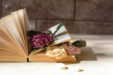 Book with beautiful dried flowers on light table, space for text