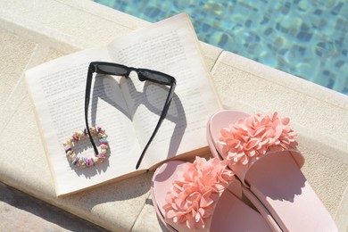 Photo of Book and different beach accessories near outdoor swimming pool on sunny day, flat lay