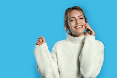 Beautiful young woman wearing knitted sweater on light blue background