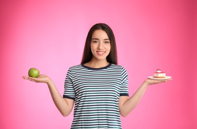 Photo of Concept of choice. Woman holding apple and cake on pink background