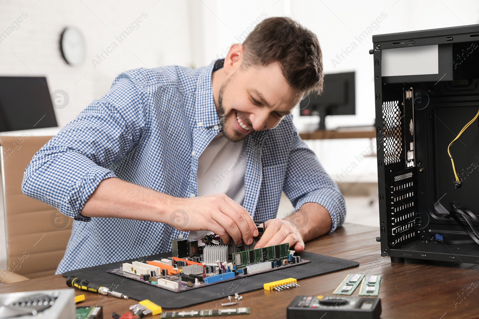 Photo of Male technician repairing motherboard at table indoors