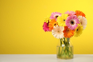 Photo of Bouquet of beautiful bright gerbera flowers in vase on table against color background. Space for text