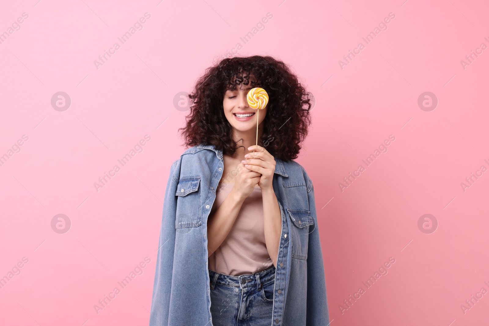 Photo of Beautiful woman covering eye with lollipop on pink background