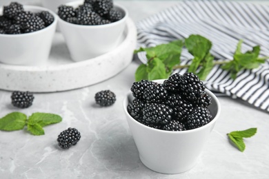 Photo of Bowl of tasty blackberries on grey marble table, space for text