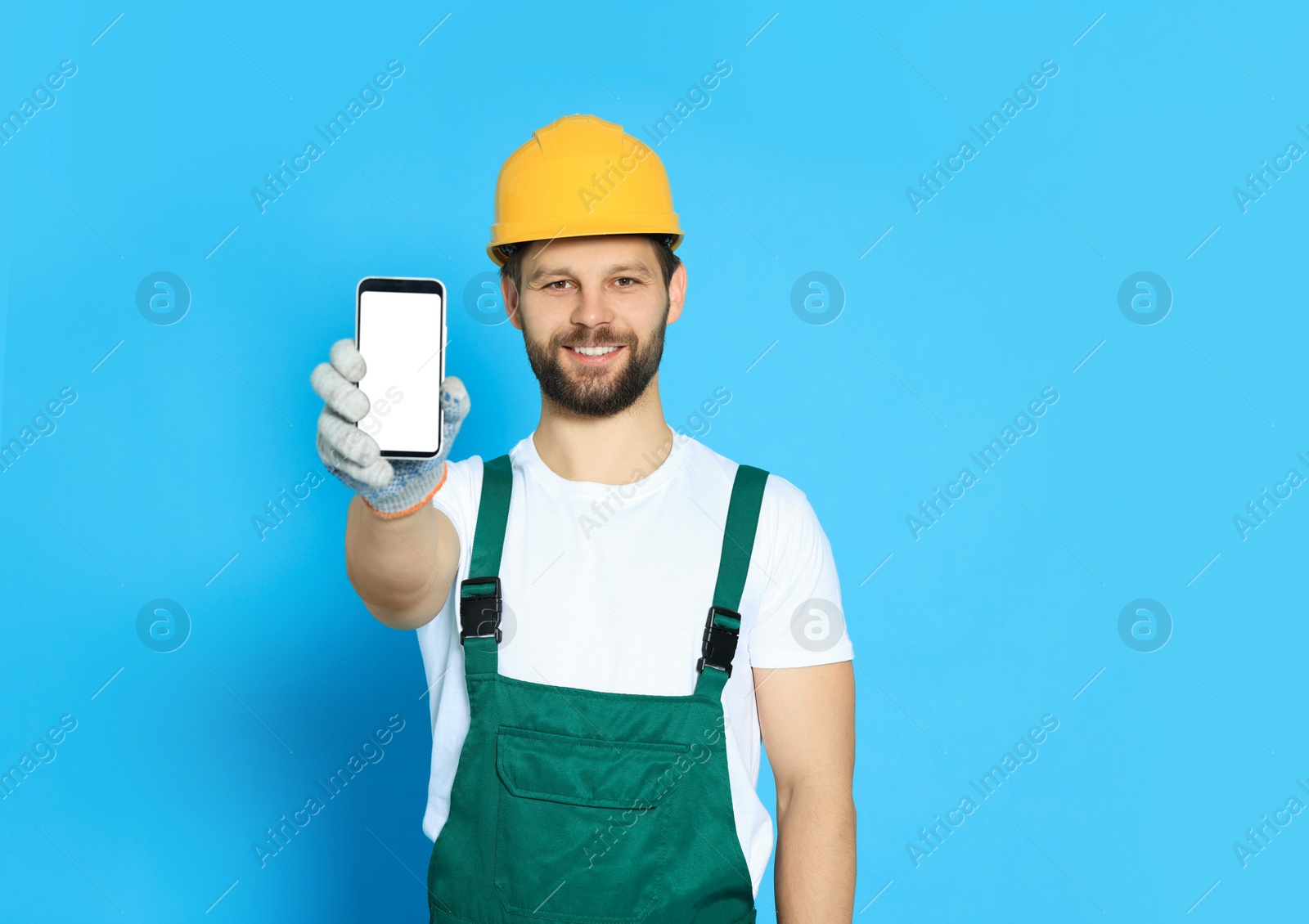 Photo of Professional repairman in uniform showing smartphone on light blue background