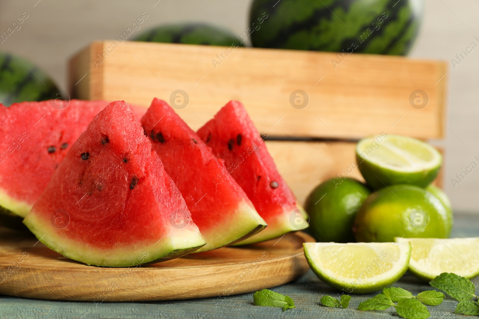 Photo of Slices of delicious watermelon, limes and mint on light blue wooden table