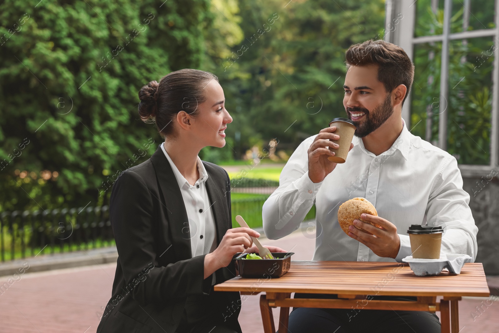 Photo of Business lunch. Happy colleagues spending time together at wooden table during break outdoors