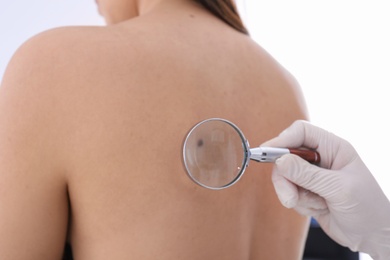 Dermatologist examining patient with magnifying glass in clinic, closeup view