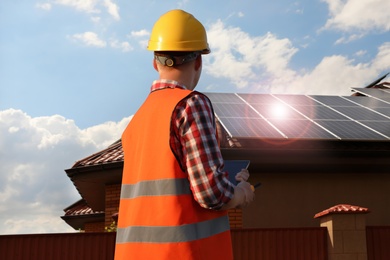 Engineer near house with installed solar panels. Alternative energy source