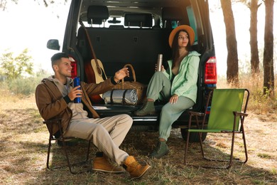 Couple resting near car and enjoying hot drink at camping site