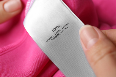 Photo of Woman reading clothing label with material content on pink shirt, closeup
